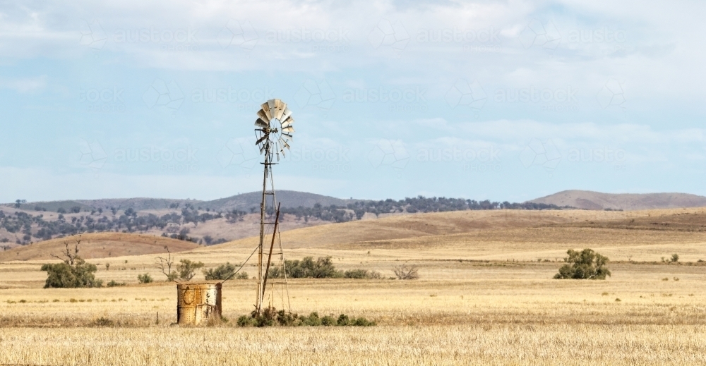 Windmill and old tank in stubble with rolling hills - Australian Stock Image