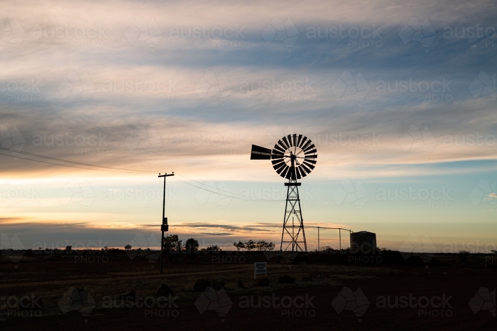 Windmill and water tank silhouetted against early evening sky with clouds - Australian Stock Image