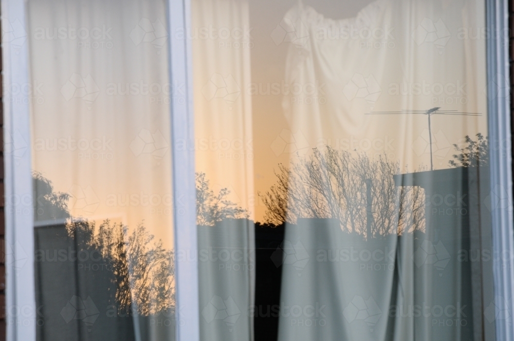Window reflection of houses and trees at sunset during winter - Australian Stock Image
