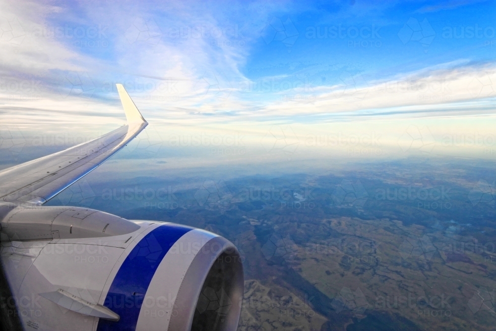 Wing and engine of aeroplane with blue sky and earth below - copy space - Australian Stock Image