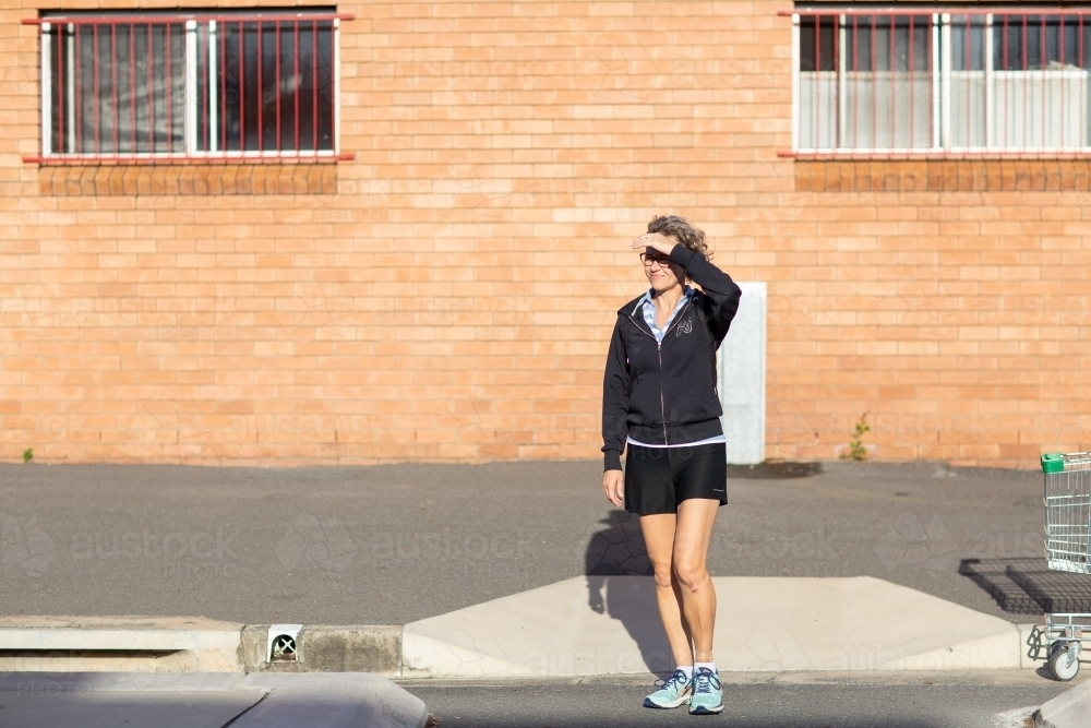 Woman about to cross the road in front of a brick building - Australian Stock Image