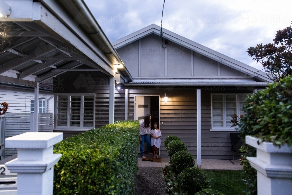 Woman and a little girl standing outside the front porch of a suburban house at night - Australian Stock Image