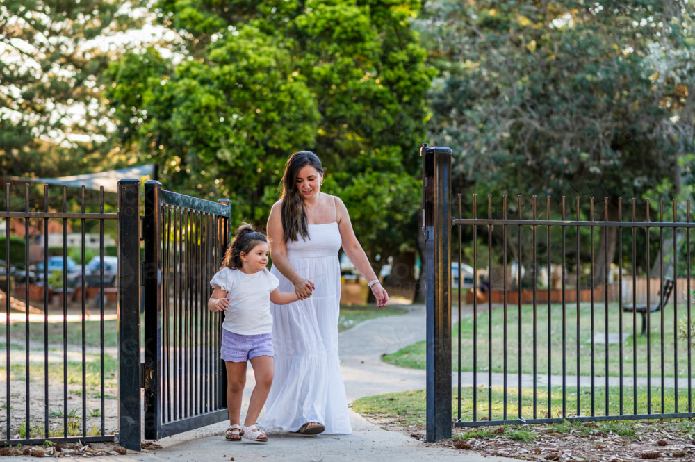 Woman and girl walk together through gate in park on a sunny day - Australian Stock Image