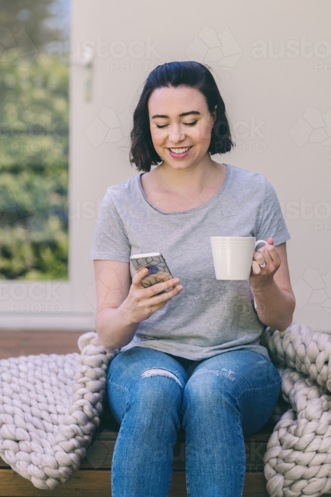 woman at home with cup of tea browsing on her phone - Australian Stock Image