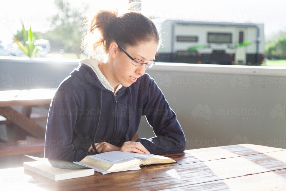 Woman at park picnic table reading a book in morning sunlight - Australian Stock Image