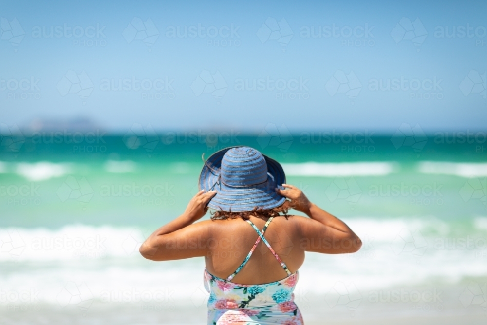 Woman at seaside holding hat on head from behind - Australian Stock Image