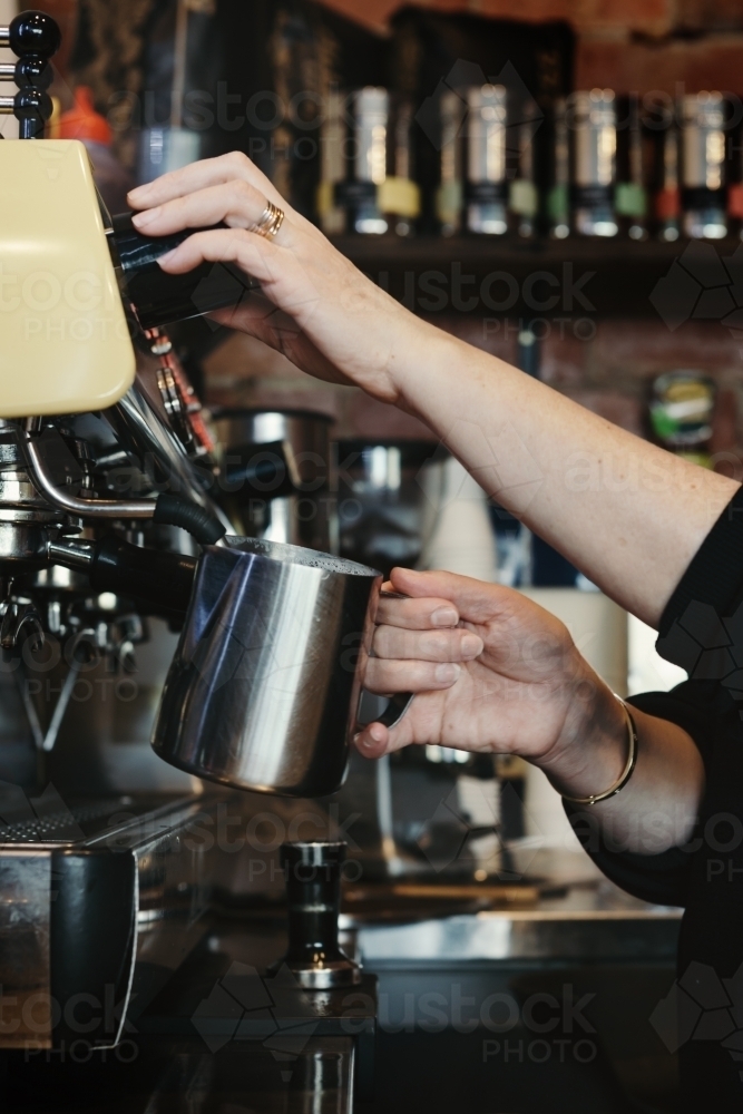 Woman barista making espresso coffee and frothing milk with steam - Australian Stock Image