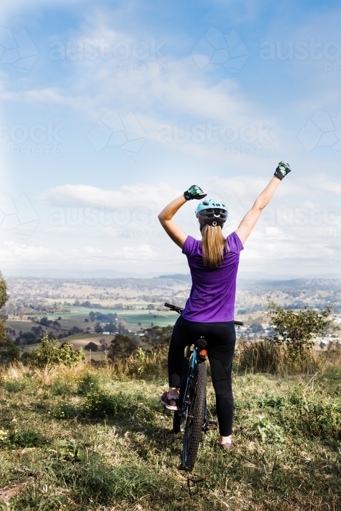 Woman biker on top of the hill celebrating achievement - Australian Stock Image