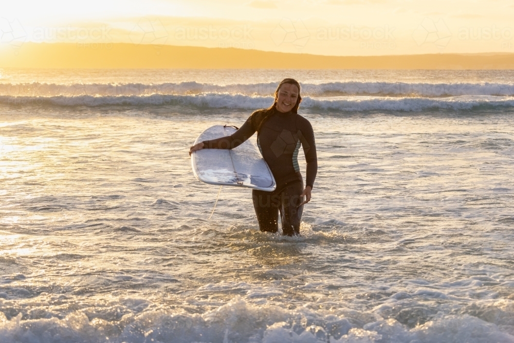 woman carrying surfboard out of the ocean - Australian Stock Image