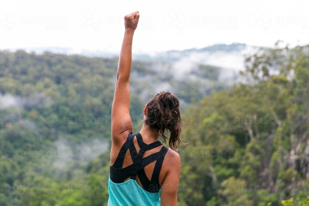 Woman celebrating achievement above a misty rainforest view below - Australian Stock Image