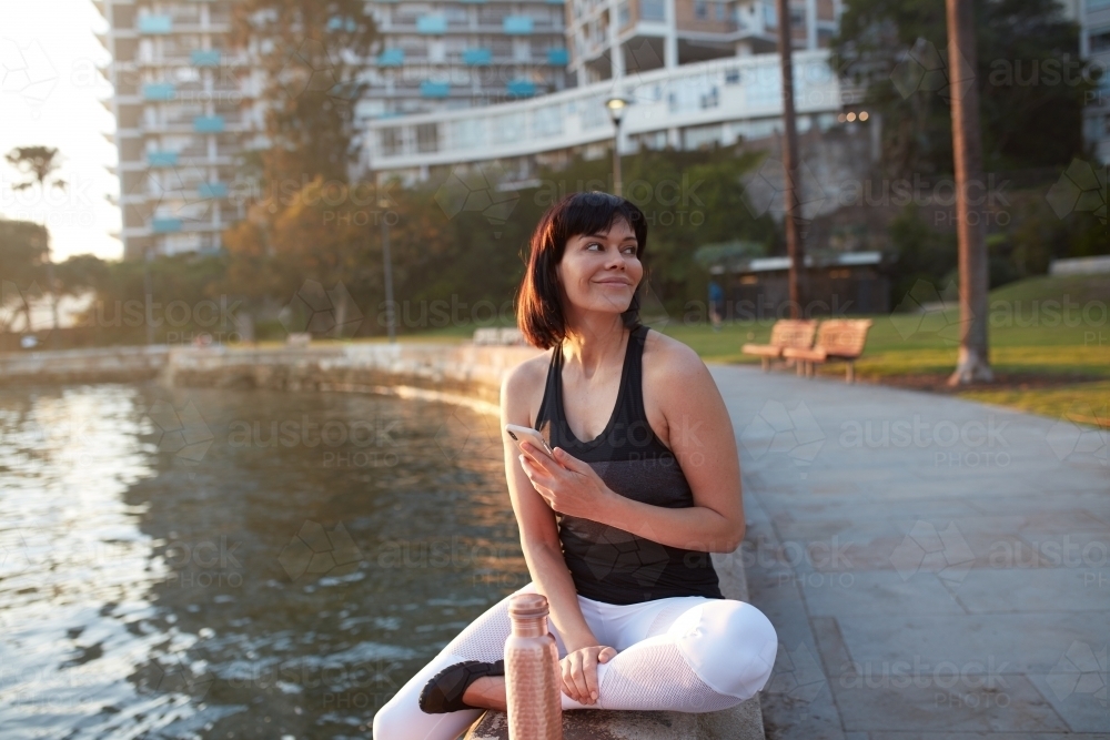 Woman checking phone by harbour at sunrise - Australian Stock Image