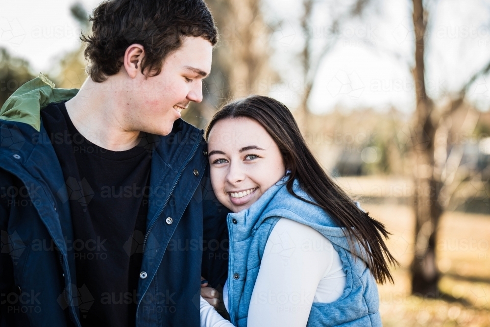 Woman cuddling into boyfriend's arm while he looks at her smiling - Australian Stock Image