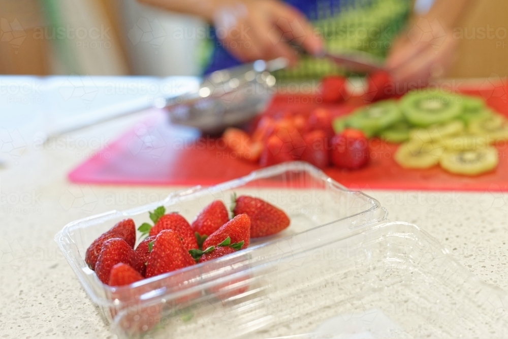 Woman cutting up strawberries and kiwi fruit on a cutting board - Australian Stock Image