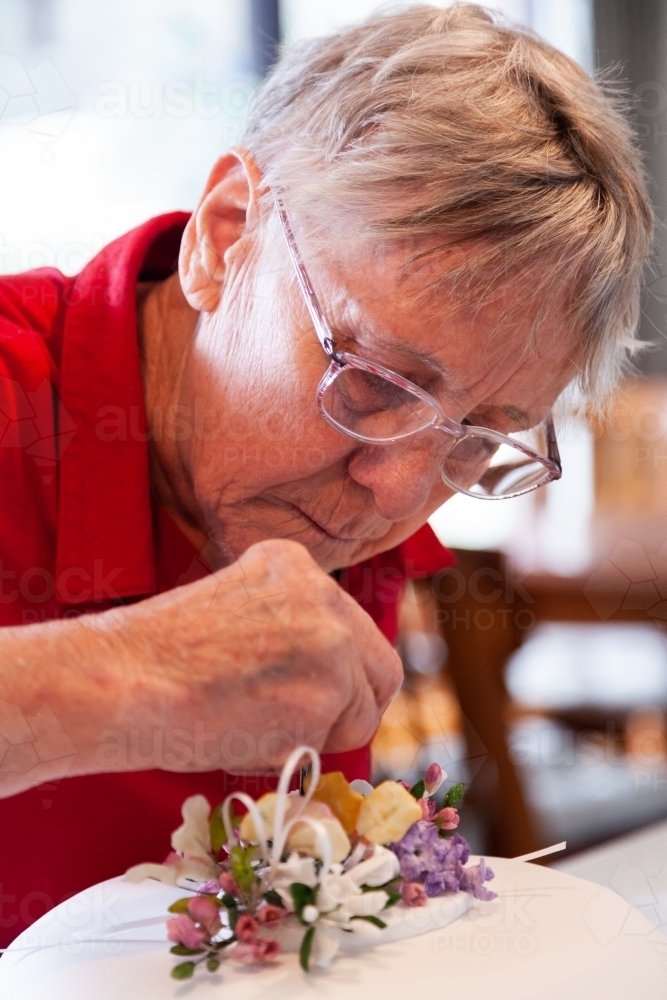 Woman decorating birthday cake with hand made native flower cake topper - Australian Stock Image