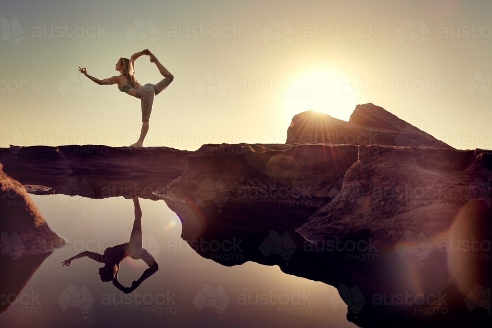 Woman doing yoga by the ocean with sun flare - Australian Stock Image