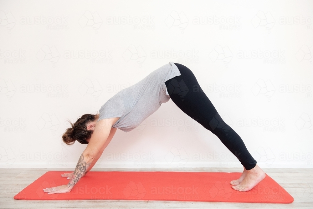 woman doing yoga downward dog pose on yoga mat in studio - Australian Stock Image