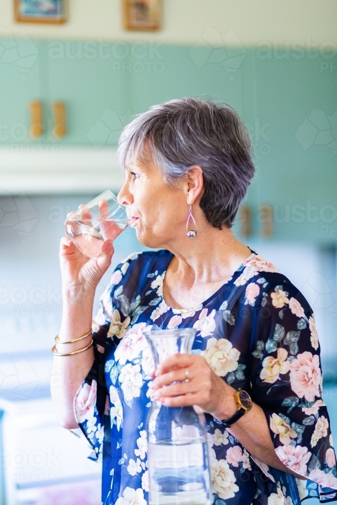 Woman drinking a glass of water in her kitchen - Australian Stock Image