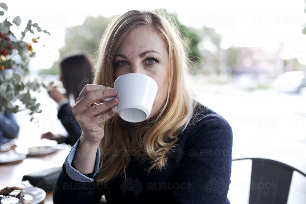 Woman drinking coffee from a mug looking straight into the camera - Australian Stock Image