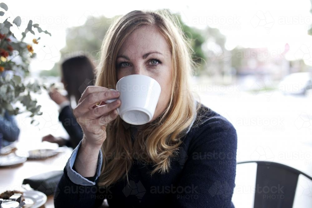 Woman drinking coffee from a mug outside cafe - Australian Stock Image