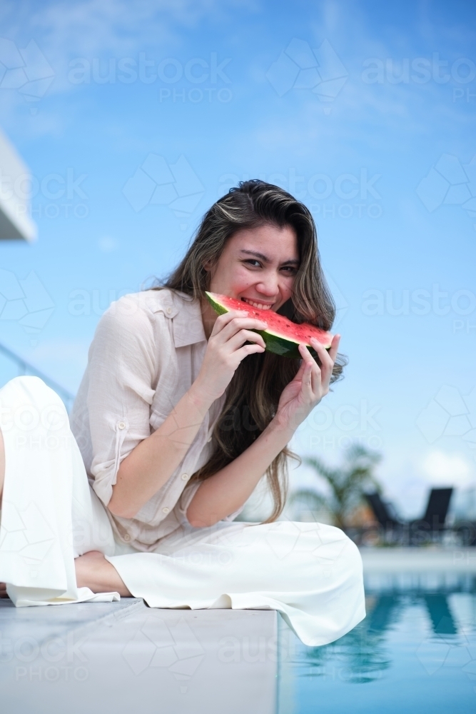 Woman eating watermelon beside pool - Australian Stock Image
