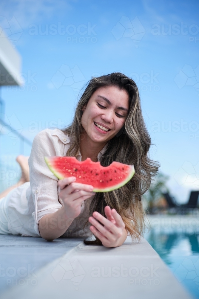 Woman eating watermelon beside pool - Australian Stock Image