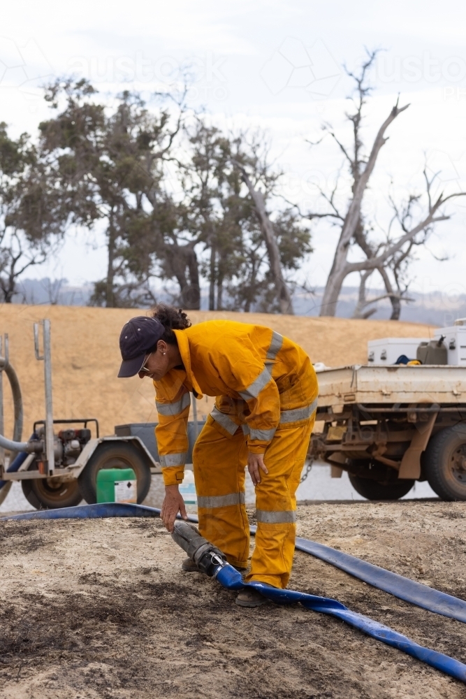 Woman firefighter bending down to connect hose at fire scene - Australian Stock Image