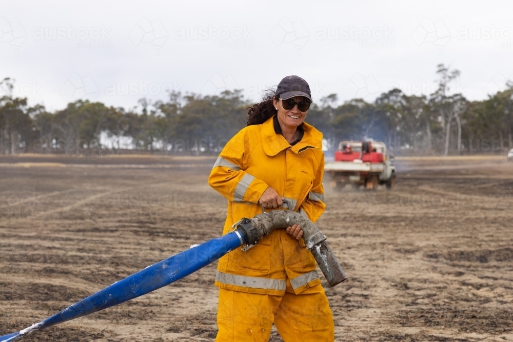 Woman firefighter pulling hose in burnt paddock - Australian Stock Image