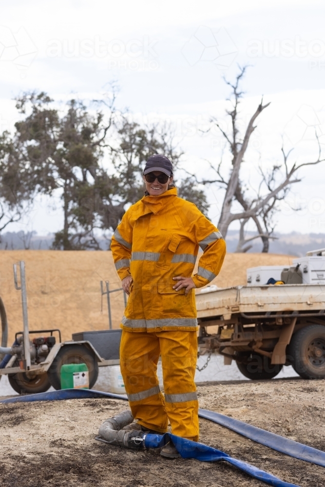 Woman firefighter smiling with hands on hips at fire scene - Australian Stock Image