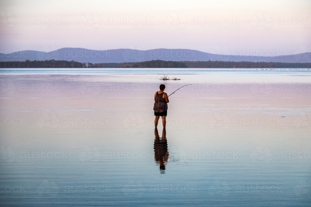 Woman fishing in lake with reflection in water - Australian Stock Image