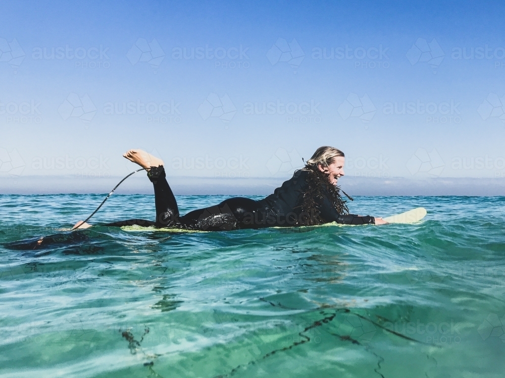 Woman floating on surfboard in wetsuit with seaweed boa - Australian Stock Image