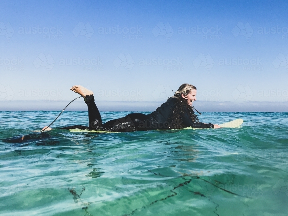 Woman floating on surfboard in wetsuit with seaweed boa - Australian Stock Image