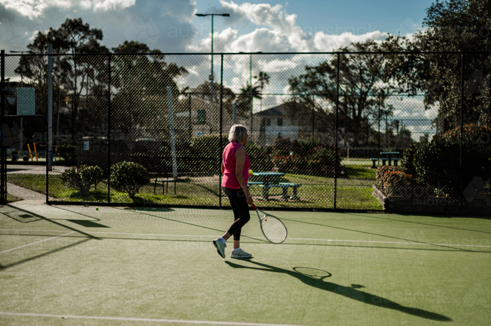 Woman has fun playing tennis outdoors on a green court under bright sunlight - Australian Stock Image