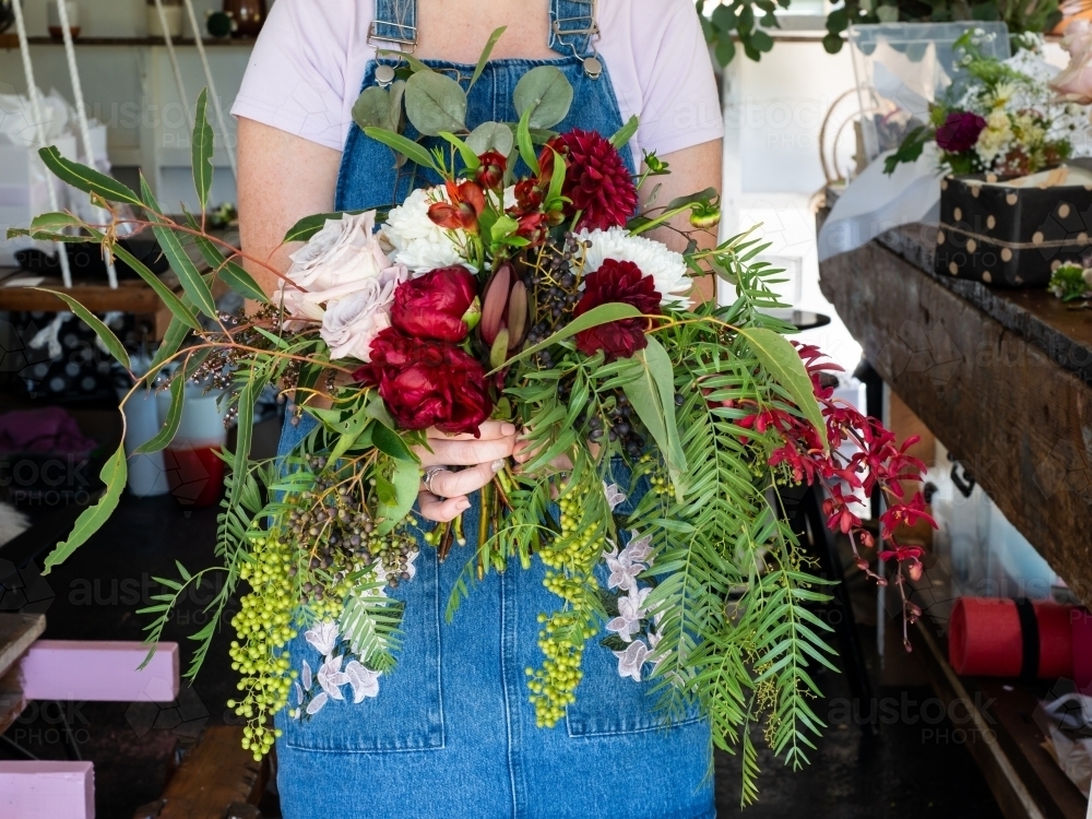 Woman holding a large floral arrangement with pink and red roses, orchids and ferns - Australian Stock Image