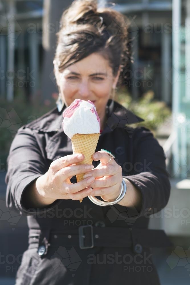 Woman holding an ice cream cone to camera - Australian Stock Image