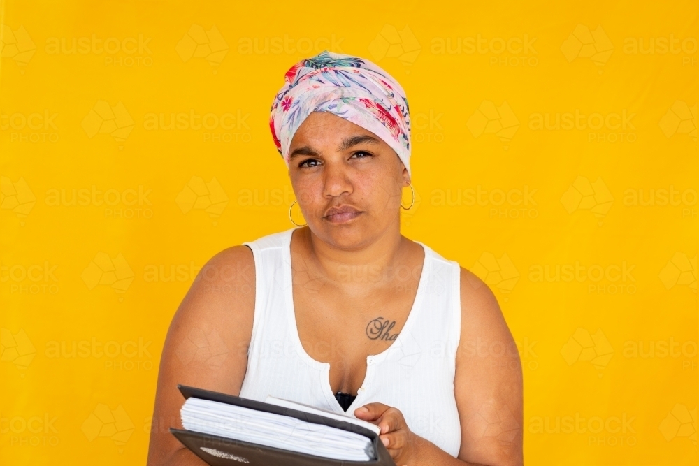 woman holding books against bright yellow background - Australian Stock Image