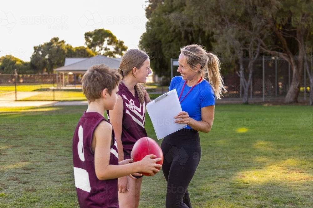 woman holding clipboard instructing children on football field - Australian Stock Image