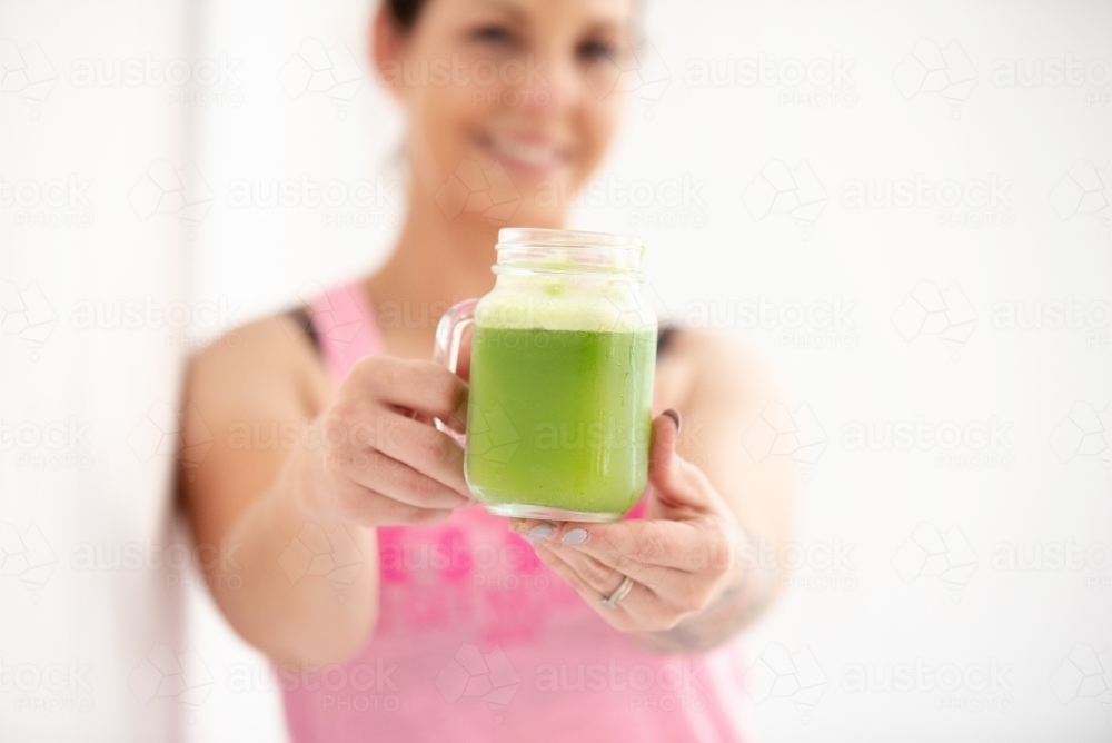 woman holding green juice in glass smiling in workout gear white background - Australian Stock Image