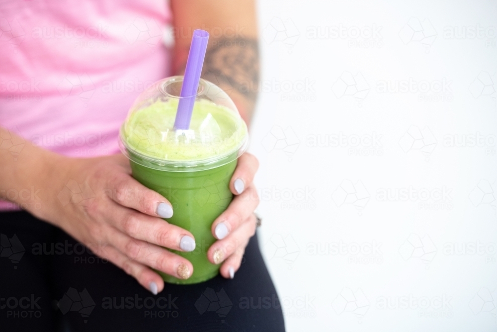 woman holding green juice in yoga workout clothes - Australian Stock Image
