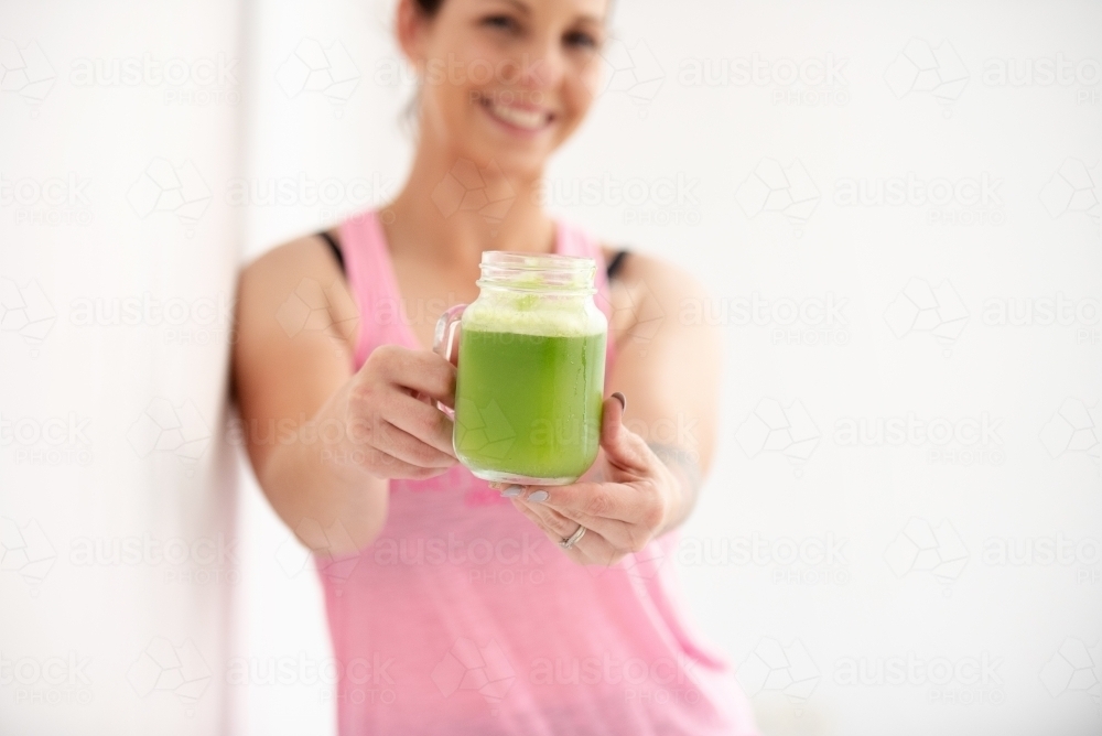 woman holding green juice smiling on white background - Australian Stock Image