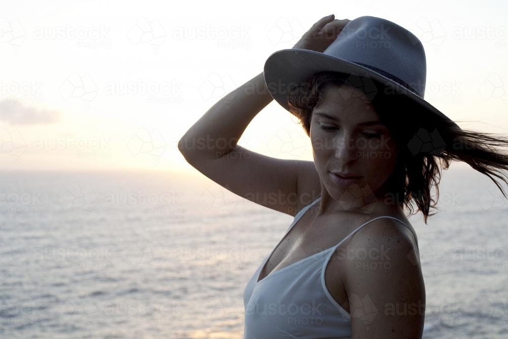 Woman holding hat with ocean in background - Australian Stock Image