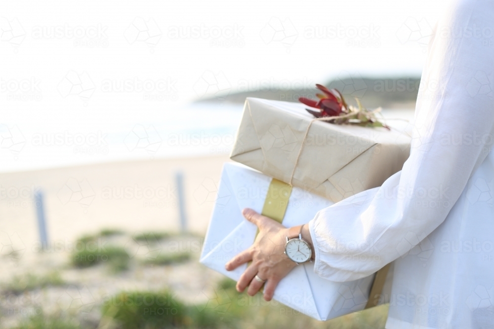 Woman holding presents with beach in background - Australian Stock Image