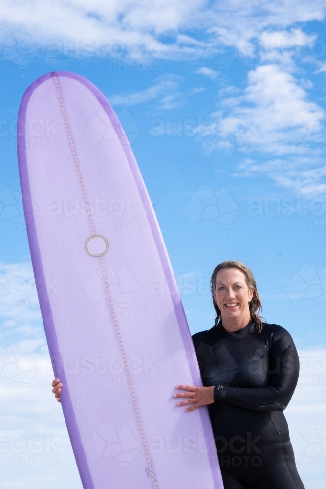 Woman holding purple longboard surfboard wearing a steamer wetsuit  with wet hair - Australian Stock Image