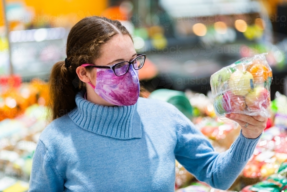 Woman holding up pack of fresh fruit covered in plastic, grocery shopping during covid - Australian Stock Image