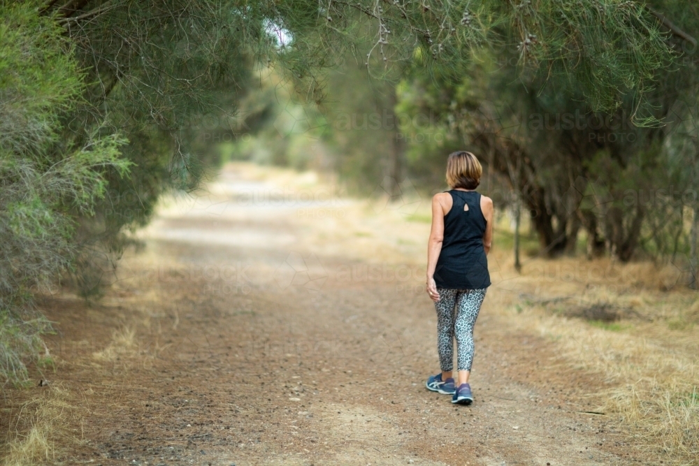 woman in activewear walking away down  country lane - Australian Stock Image