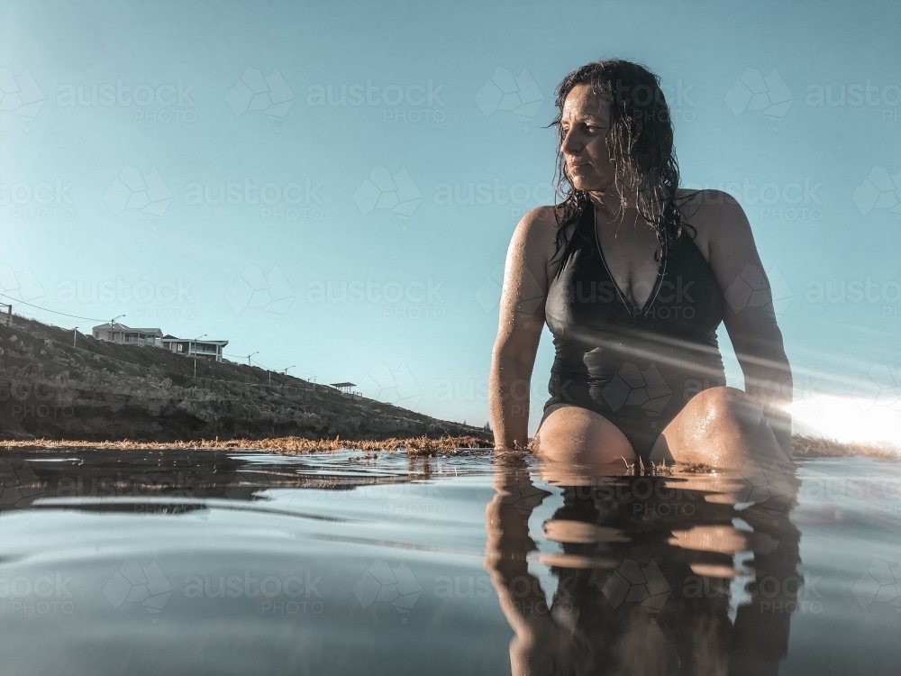 Woman in black bathing suit posing on waters edge in calm ocean - Australian Stock Image