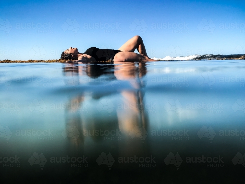 Woman in black bathing suit posing on waters edge in calm ocean - Australian Stock Image