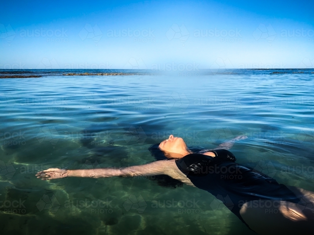 Woman in black bathing suit posing on waters edge in calm ocean - Australian Stock Image