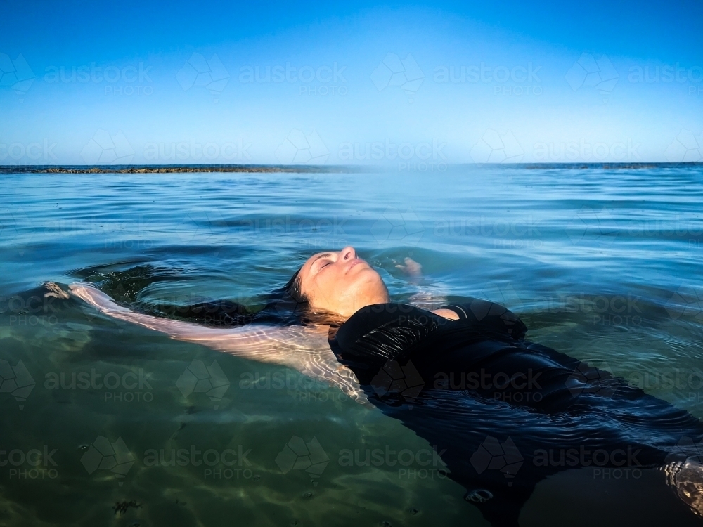 Woman in black bathing suit posing on waters edge in calm ocean - Australian Stock Image