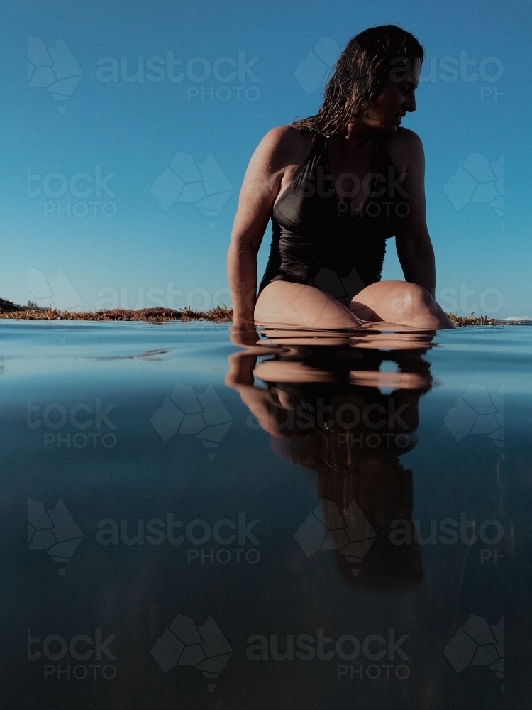 Woman in black bathing suit posing on waters edge in calm ocean - Australian Stock Image