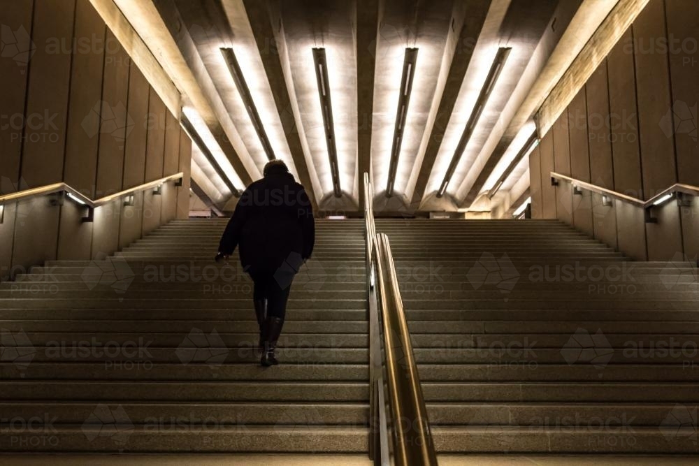 Woman in black walking up dimly lit stairs - Australian Stock Image